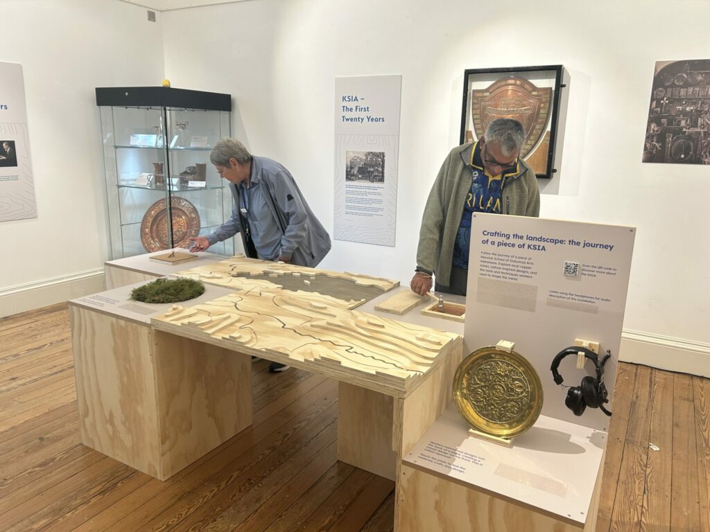 Two people study a museum installation comprised on objects and surfaces to touch and handle