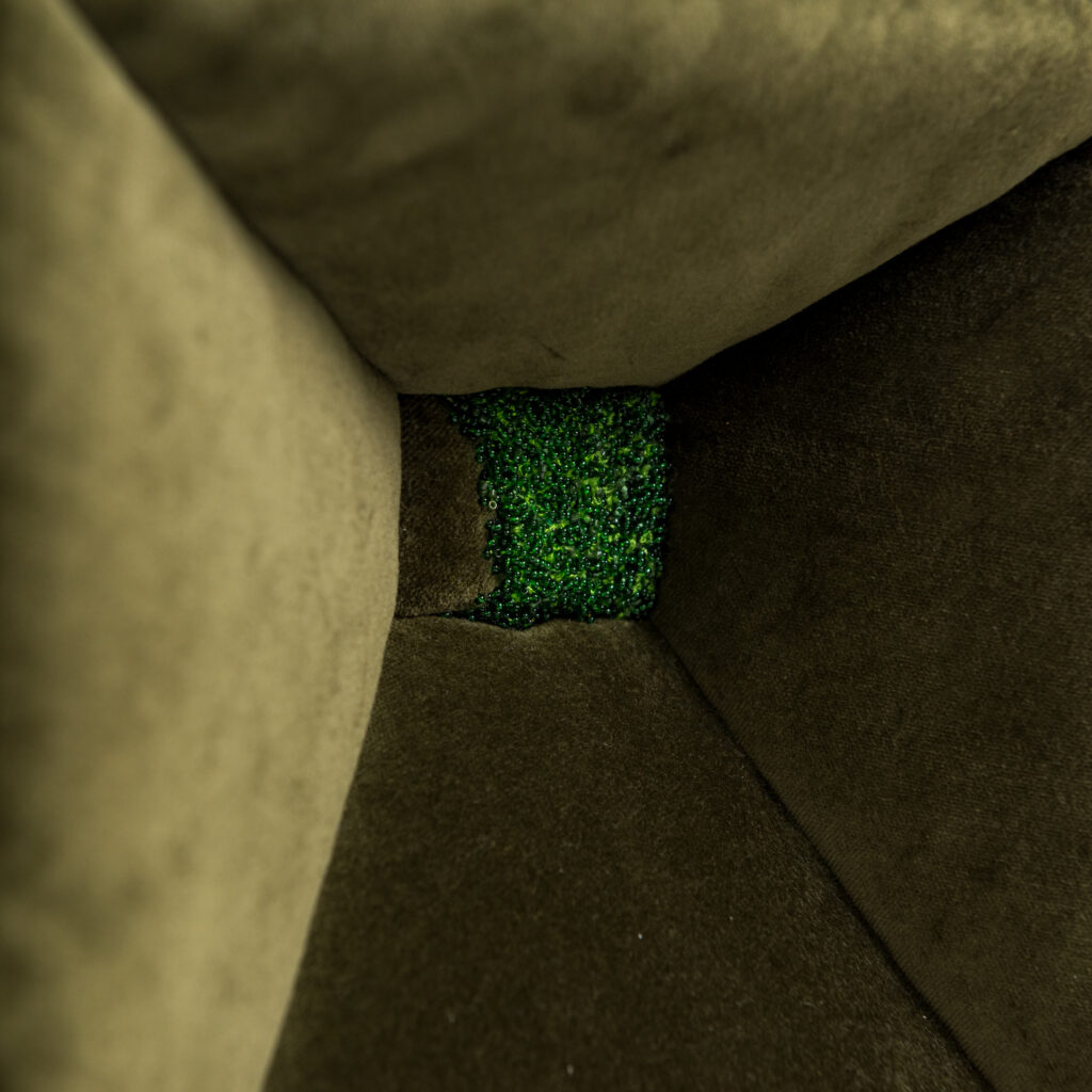 The sides of a box, upholstered in green velvet, decrease to a small rectangle, partially covered in tiny green beads