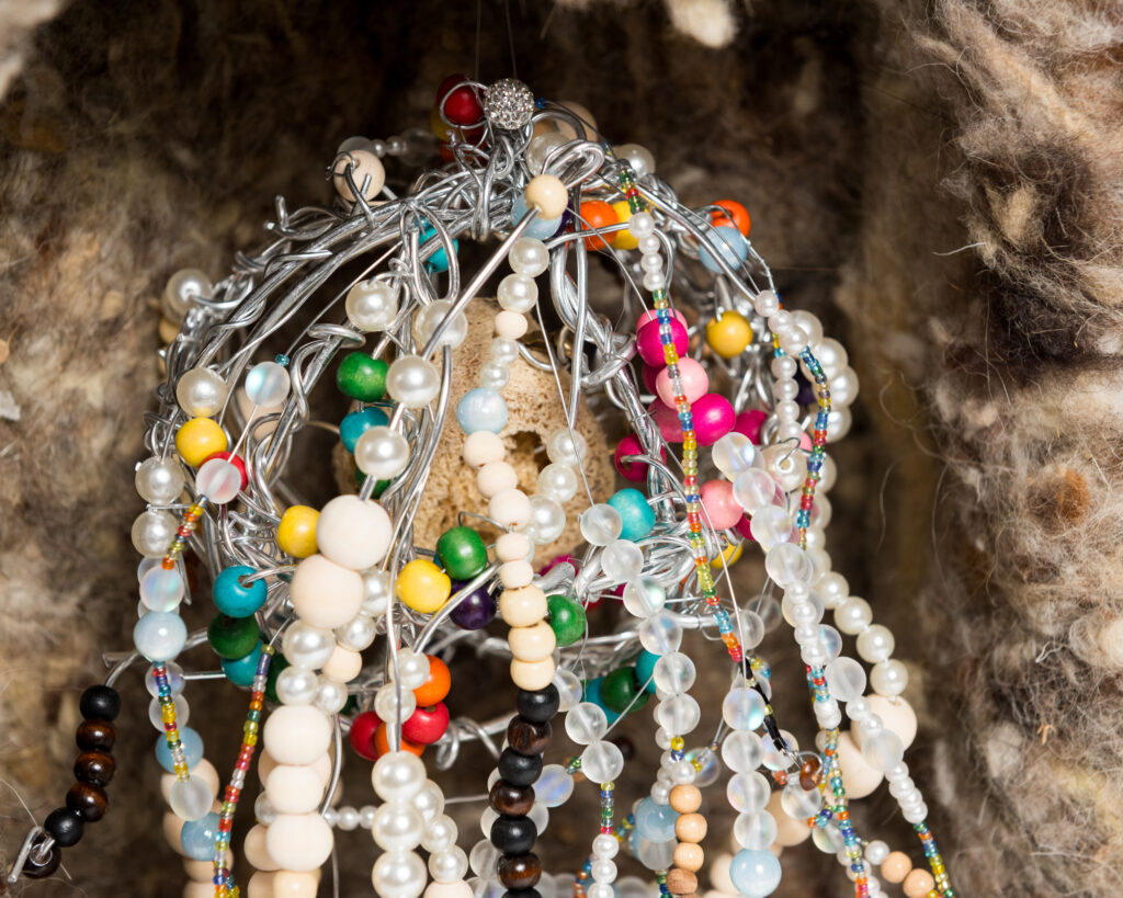 Multicoloured beads strung on to a tangle bendy wires which hang in a bunch within a raw wool-lined box