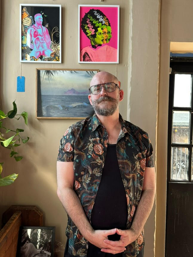 A white man with a beard wearing aviator style glasses and a brown flowery shirt.