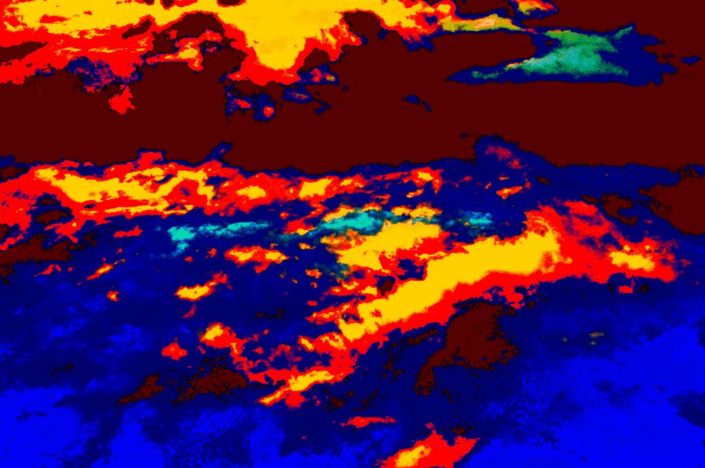 A heavily edited photograph of a cloudy sky at sunset with fiery red and yellows, and shades of blue. 