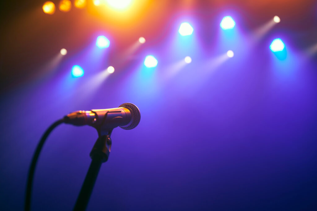 Selective focus on lluminated microphone on stage against colourful spotlights.