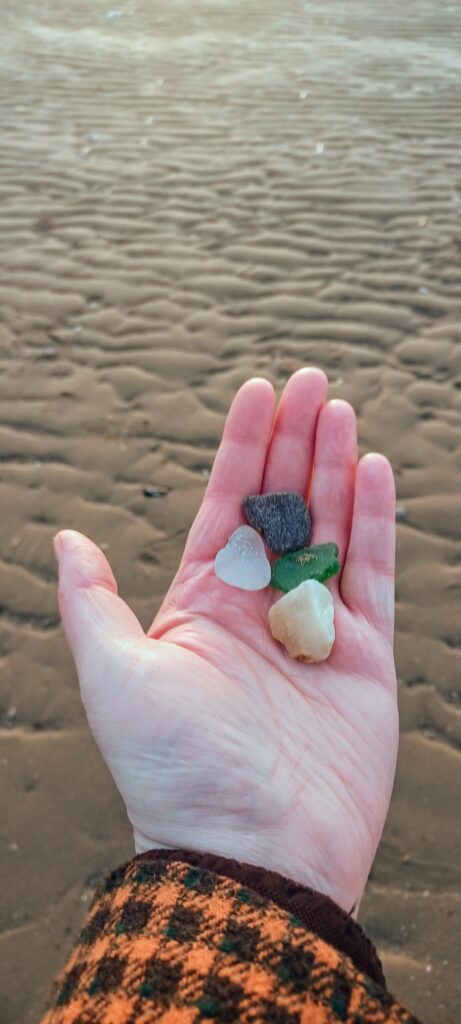 Photograph of a hand holding some sea glass on a beach